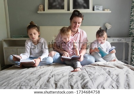 Casual Caucasian mother reads a book with three children in bed in bedroom, mother with her children, spending time together and caring at home, sibling relationships and difficulties with children