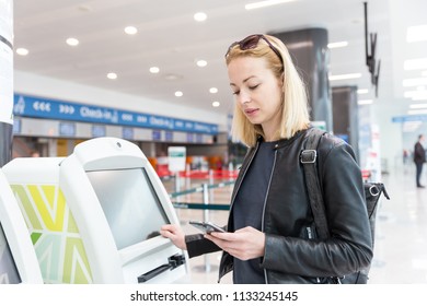 Casual caucasian woman using smart phone application and check-in machine at the airport getting the boarding pass. Modern technology on airport.