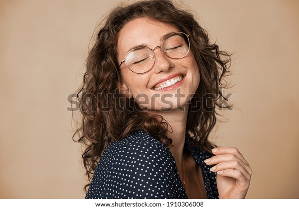 Casual cheerful woman with eyeglasses smiling at\
camera on cream background. Close up of happy young woman laughing\
with eyeglasses. Beautiful girl having fun with closed eyes showing\
a big grin.