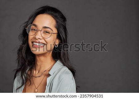 Casual cheerful young woman with eyeglasses smiling at camera on gray background. Close up face of happy multiethnic girl laughing with trendy eyeglasses and copy space. Beautiful mixed race girl.