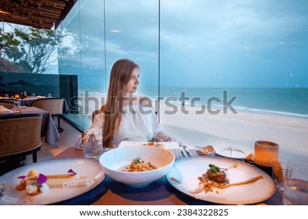 Casual chic dressed female diner experiencing fine eating, tranquil beachside setting, sophisticated culinary delight.
