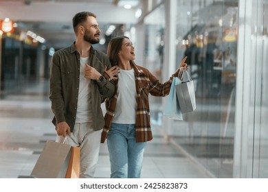 In casual clothes, with bags, shopping. Young couple are in supermarket together. - Powered by Shutterstock