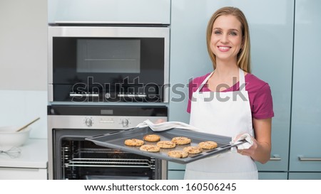 Casual content woman holding baking tray with cookies in bright kitchen