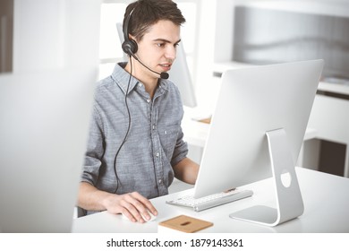 Junge Männer, die mit Headset und Computer gekleidet sind, während sie online mit Kunden sprechen. Call-Center, Business-Konzept