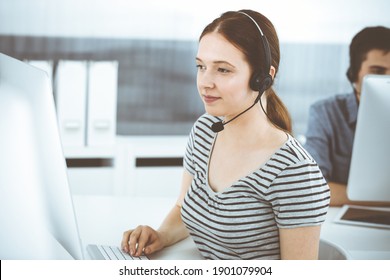 Casual Dressed Young Woman Using Headset And Computer While Talking With Customers Online. Group Of Operators At Work. Call Center, Business Concept