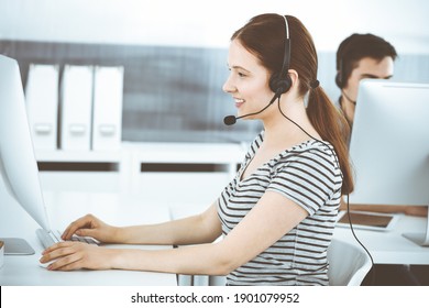 Casual Dressed Young Woman Using Headset And Computer While Talking With Customers Online. Group Of Operators At Work. Call Center, Business Concept