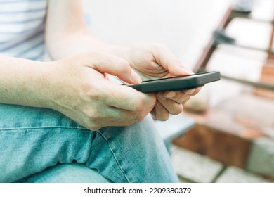 Casual Female Person Wearing Jeans Trousers Using Smartphone Device Outdoors While Sitting On The Bench In House Back Yard, Selective Focus