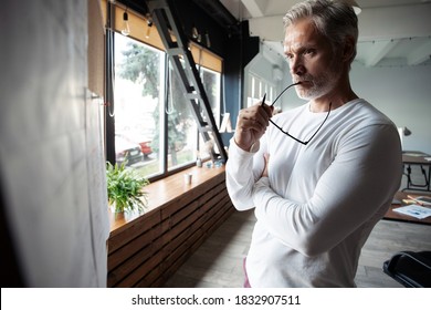 Casual Grey-haired Mature Handsome Man Looking At His Ideas Written On Paper And Stuck To A Wall.