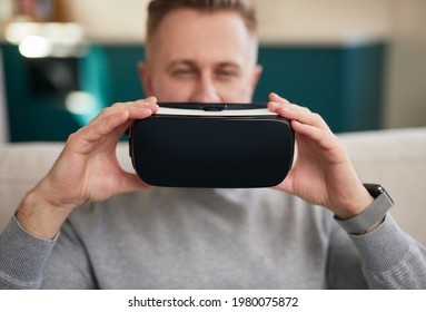 Casual Guy In Gray Sweatshirt Putting On VR Goggles While Sitting On Sofa At Home