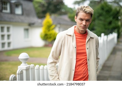 casual handsome man stand in front of suburaban home in a village while being confident and relaxed with his youth and smart lifestyle and look flirty and coquettish at camera