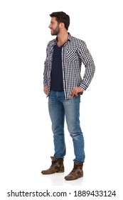 Casual handsome man is standing, holding hands on hip, smiling and looking away. Full length studio shot isolated on white.