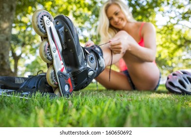 Casual Happy Blonde Putting On Roller Blades In A Park