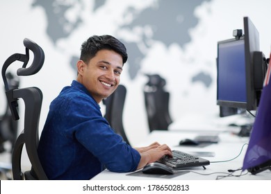 casual indian business man working on desktop computer in modern open plan startup office interior