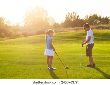 Casual kids at a golf field holding golf clubs. Sunset