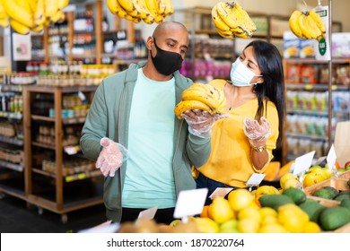 Casual Latin American Family Couple In Protective Face Masks To Prevent Viral Infection Shopping Together In Fruit And Vegetable Section Of Supermarket. New Lifestyle In Pandemic