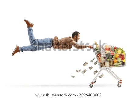 Casual man flying and holding onto a shopping cart with food and money isolated on white background