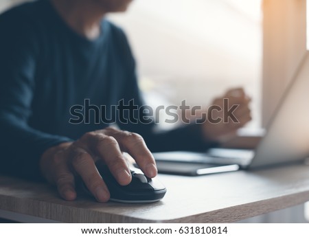 Casual man, freelance working on laptop computer and clicking wireless digital mouse with digital tablet on office table, close up, dark tone