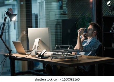 Casual man having phone call late in office while drinking energizing coffee at table.  - Powered by Shutterstock