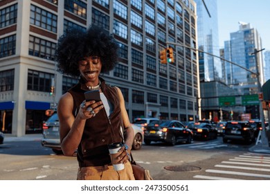 Casual man laughs while using his smartphone on a busy city street corner during the evening