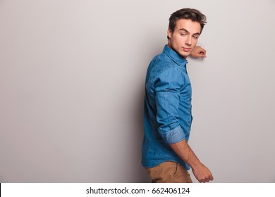 casual man leaning on grey wall looks back over his shoulder in studio - Powered by Shutterstock