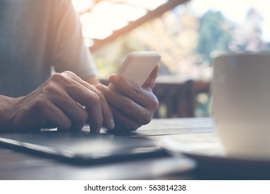 Casual man relaxed using smart phone and digital tablet with coffee cup at home, young man browsing on smart phone in interior, e business internet of things IoT concept, flare light - Powered by Shutterstock