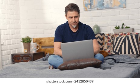 Casual man sitting on bed working online from home with laptop computer. Stay at home and work in home office. - Powered by Shutterstock