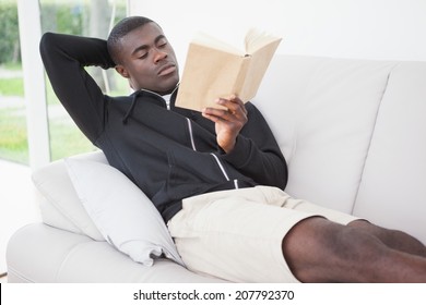 Casual Man Sitting On His Sofa Reading A Book At Home In The Living Room