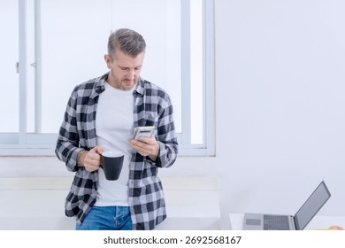 Casual Middle-aged Man Checking His Smartphone While Taking a Coffee Break From Working on His Laptop