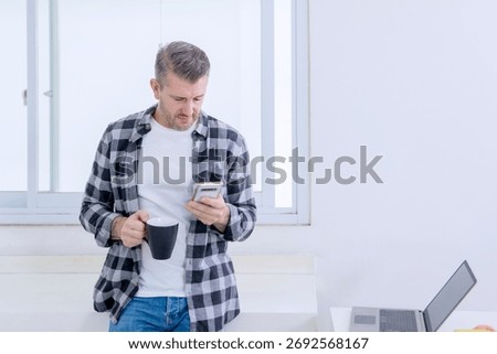 Casual Middle-aged Man Checking His Smartphone While Taking a Coffee Break From Working on His Laptop
