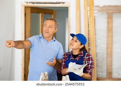 Casual middle-aged man discussing the future construction site with the female repairer in uniform in the house - Powered by Shutterstock