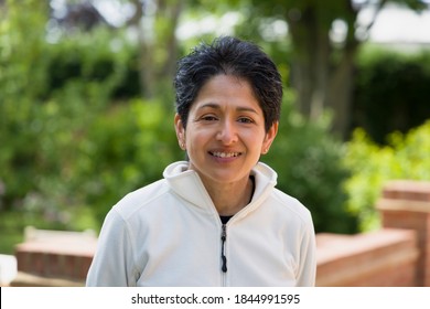 Casual portrait of an Indian woman smiling. British Asian (BAME) standing outdoors in a garden, UK