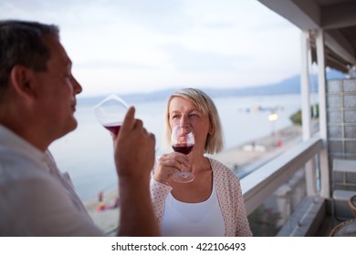 Casual Portrait of Mature Couple Drinking Red Wine Together on Balcony of Beachfront Hotel Resort - Man and Woman Toasting Vacation at Dusk - Powered by Shutterstock