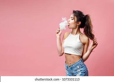 Casual pretty woman standing and vaping on pink background in studio.