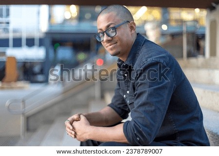 Casual smart latin businessman sitting on stairs in the city looking and smiling at camera