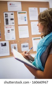 Casual Student Taking Notes In Front Of Notice Board In School