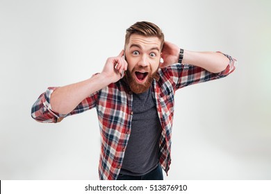 Casual Surprised Man In Plaid Shirt Talking On Mobile Phone And Looking At Camera Over White Background