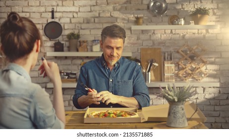 Casual White Couple Eating Take Away Pizza From Food Box At The Table In Kitchen At Home.