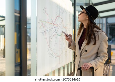 Casual Woman In Hat And Coat At A Public Transport Stop Looking At The Timetable
