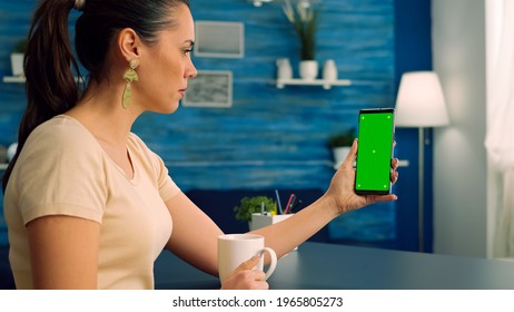 Casual Woman Having Videocall With Her Collegue While Drinking Cup Of Coffee Using Mock Up Green Screen Chroma Key Phone. Caucasian Female Working On Social Media Project Sitting On Office Desk