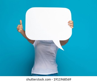 Casual Woman Hiding Behind A Speech Bubble And Giving A Thumbs Up Against Blue Background