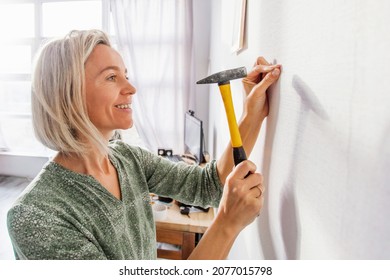 Casual woman hitting a nail in a wall with a hammer. Independent middle-aged woman does housework, repairs
 - Powered by Shutterstock