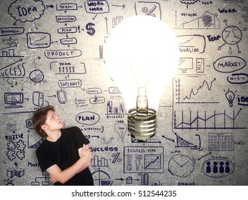 Casual young guy looking at abstract huge lamp on concrete background with creative financial sketch. Business idea concept - Shutterstock ID 512544235