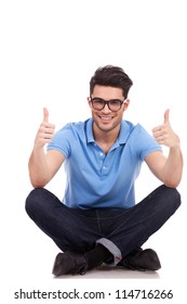 Casual Young Man Sitting Cross Legged Showing Thumbs Up With Both Hands And Smiling To The Camera