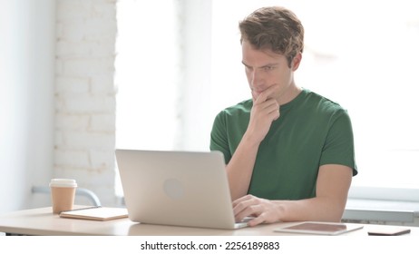 Casual Young Man Thinking while Working on Laptop