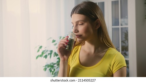 Casual young woman cooking in kitchen choosing spice to add to the dish. Housewife holding a small glass jar with dried herbs inside, enjoying the pleasant smell. - Shutterstock ID 2114505227