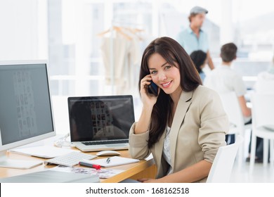 Casual young woman on call at desk with group of colleagues behind in a bright office - Shutterstock ID 168162518