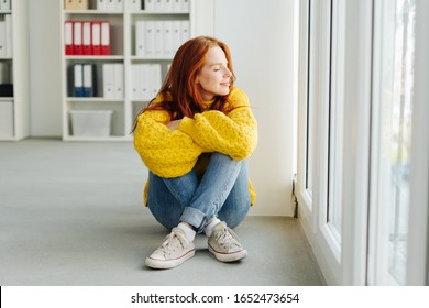 Casual young woman relaxing at the office sitting on the floor in front of a glass door facing outside with closed eyes and a blissful smile - Shutterstock ID 1652473654
