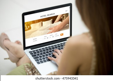 Casual Young Woman Sitting On Sofa With Notebook, Working On Laptop Computer, Searching For Lodging Using On-line Web Service, Booking A Hotel On Website. Closeup View Over The Shoulder