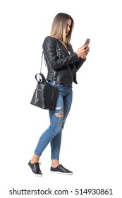 Casual Young Woman In Street Style Clothing Walking And Typing On Mobile Phone. Full Body Length Portrait Isolated Over White Background