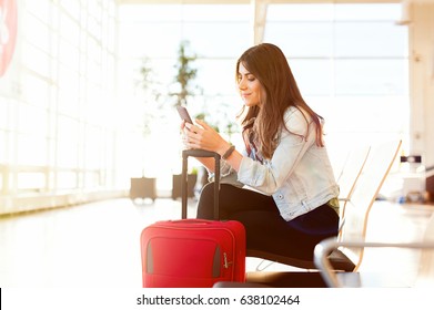 Casual Young Woman Using Her Cell Phone While Waiting To Board A Plane At The Departure Gate.